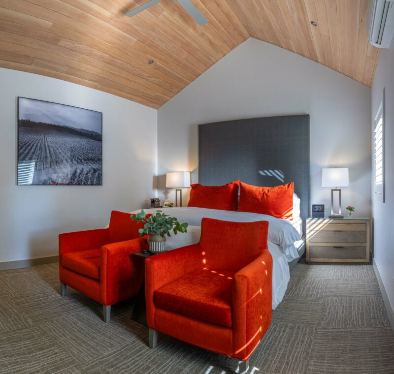 a bed room with a neatly made bed and two orange chairs