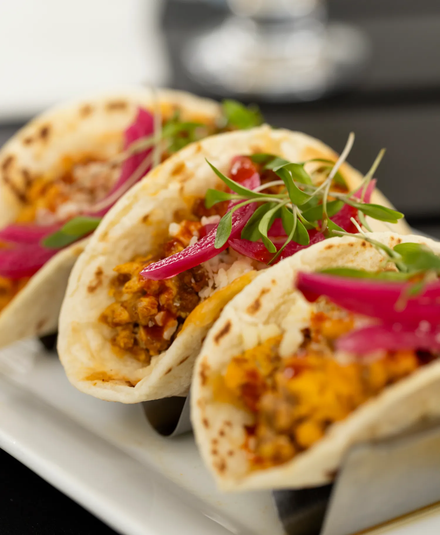 a white plate topped with three tacos covered in meat and veggies