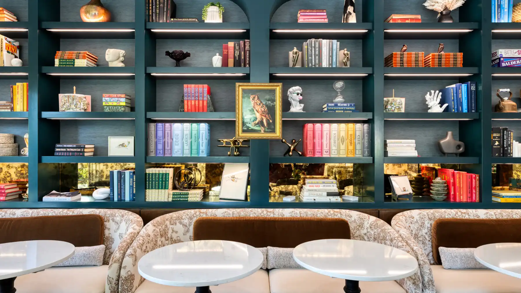 Teal bookshelves displaying colorful books and sculptures above seating areas inside SENZA Hotel.