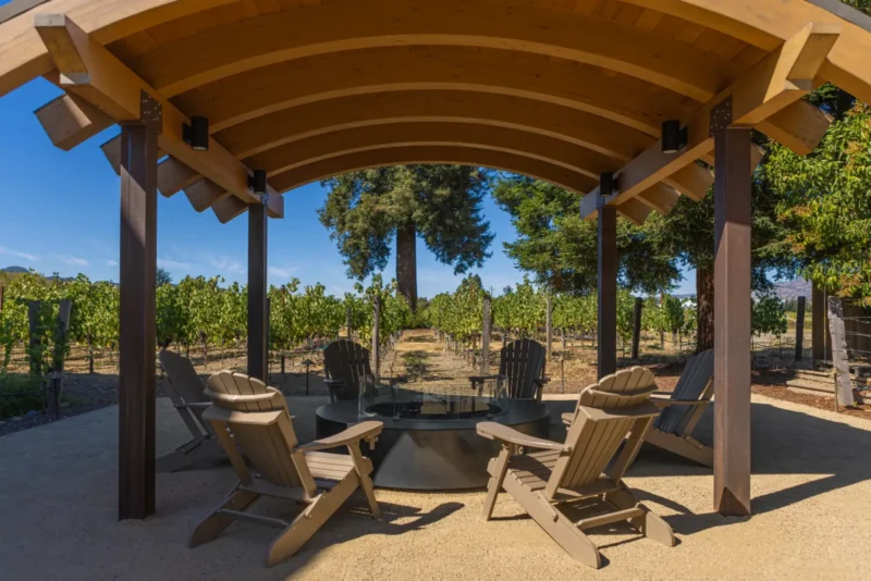 Fire pit lounge area with Adirondack chairs under a wooden arbor overlooking vineyards at a hotel in Napa Valley.