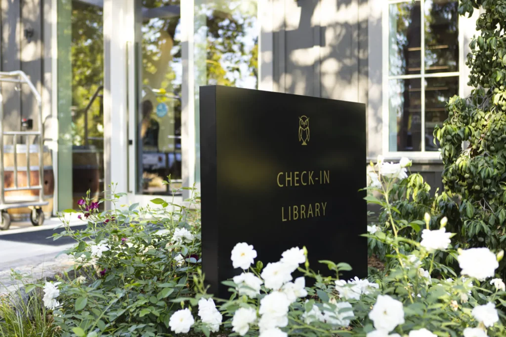 a sign in front of a library surrounded by flowers