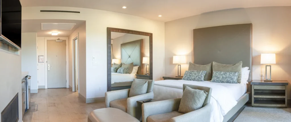 a bedroom with a bed, mirror, and two chairs