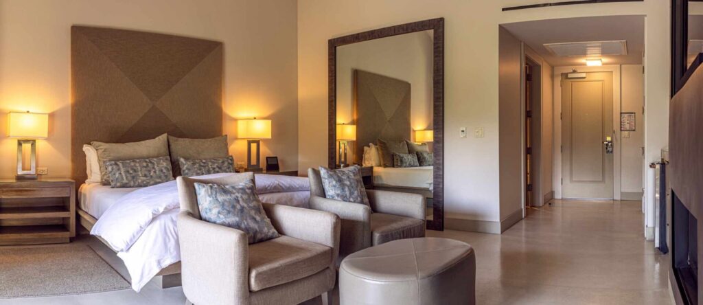 a bedroom with a bed, chair, ottoman and mirror