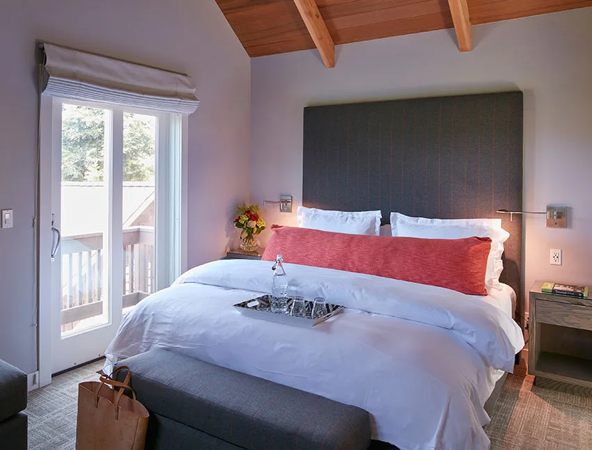 Cozy hotel bedroom with king bed, wooden ceiling, and balcony access