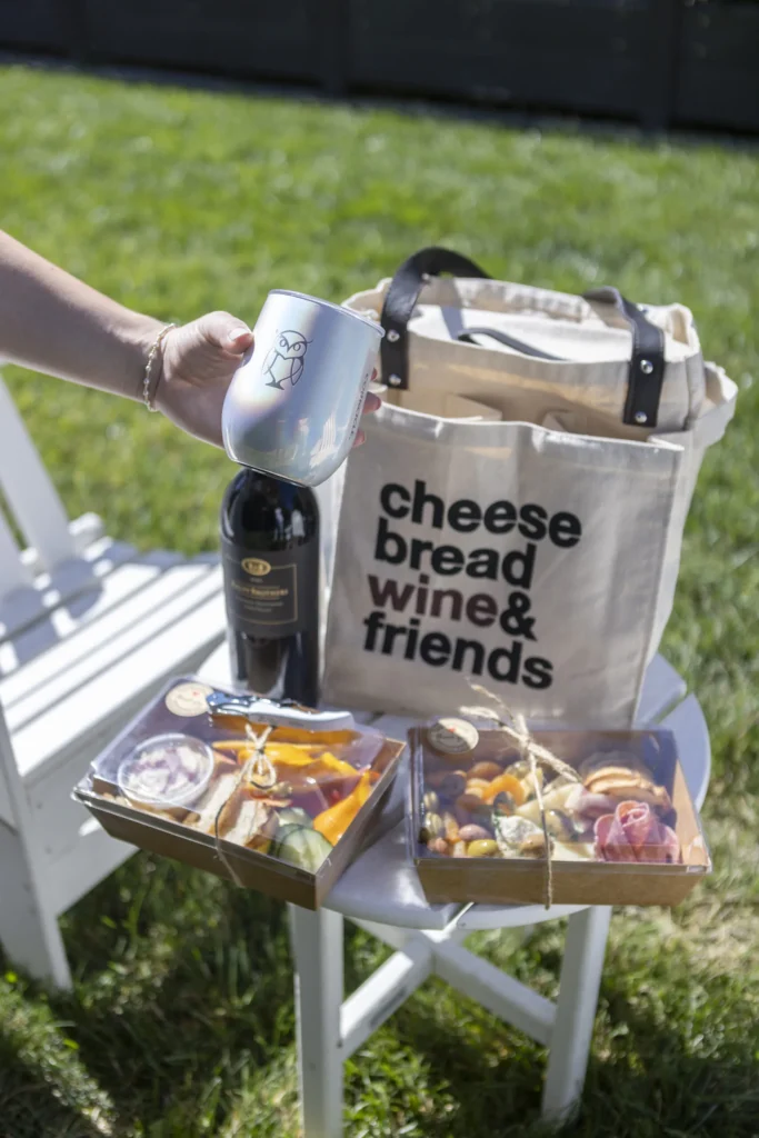 Picnic basket with cheese, bread, wine, and friends text on a white table outdoors.