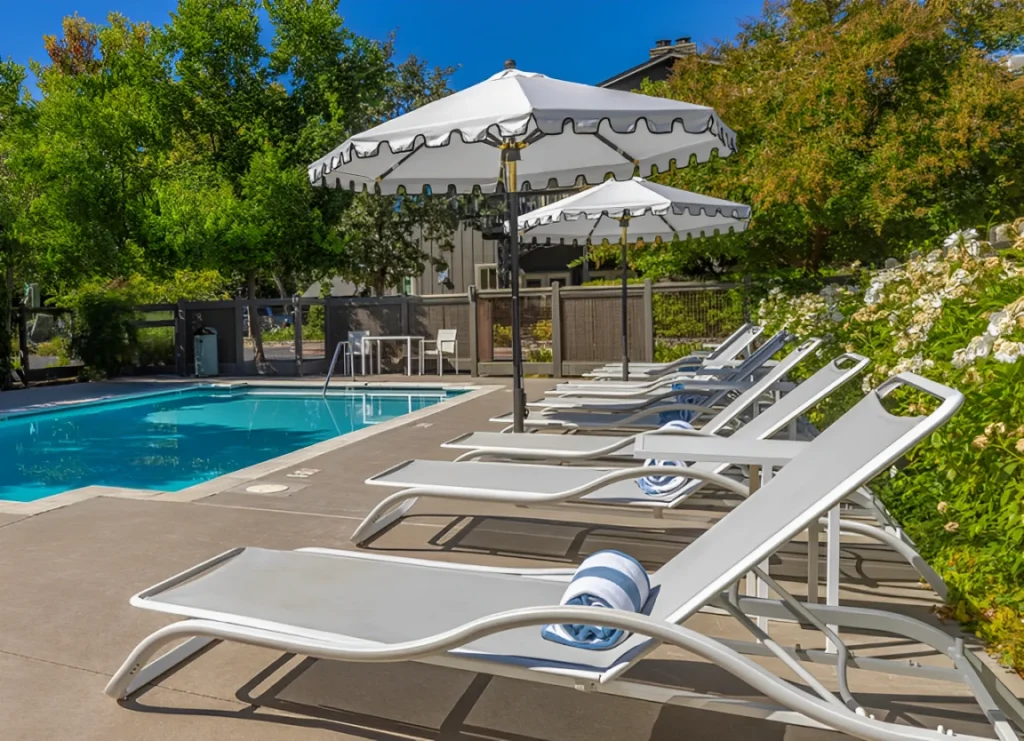 Modern lounge chairs and decorative white umbrellas line the sparkling swimming pool at hotels in Napa CA.