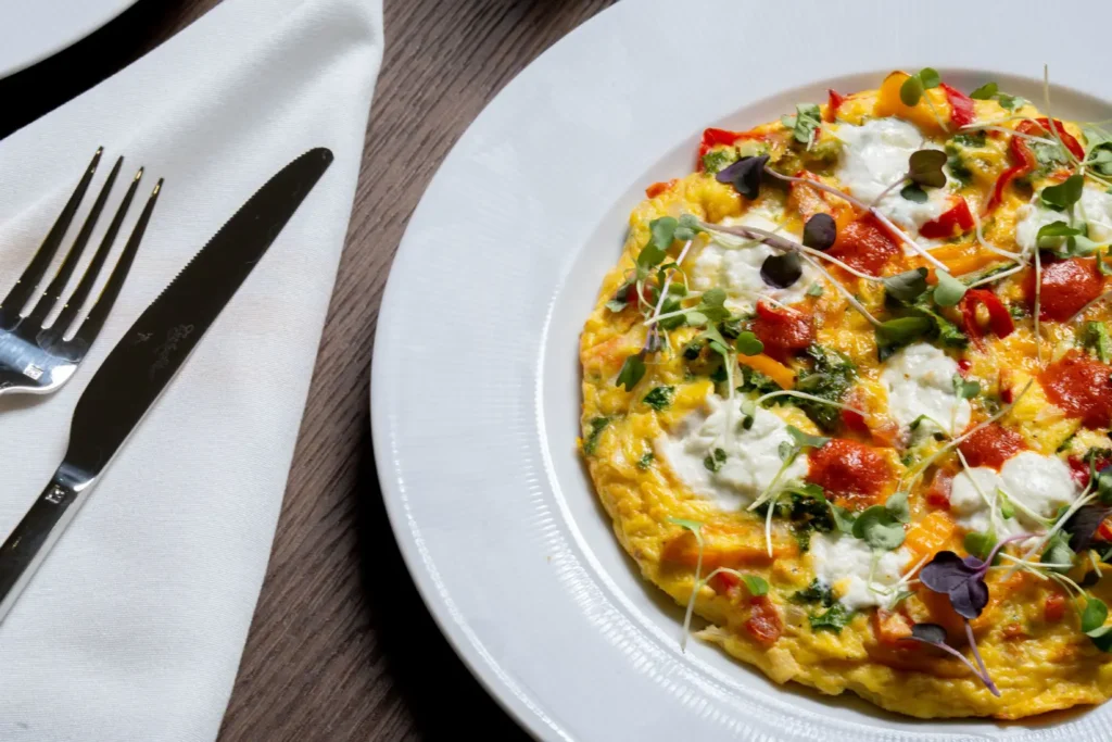 A fluffy omelet with melted white cheese, red peppers, and fresh microgreens served on a white plate.