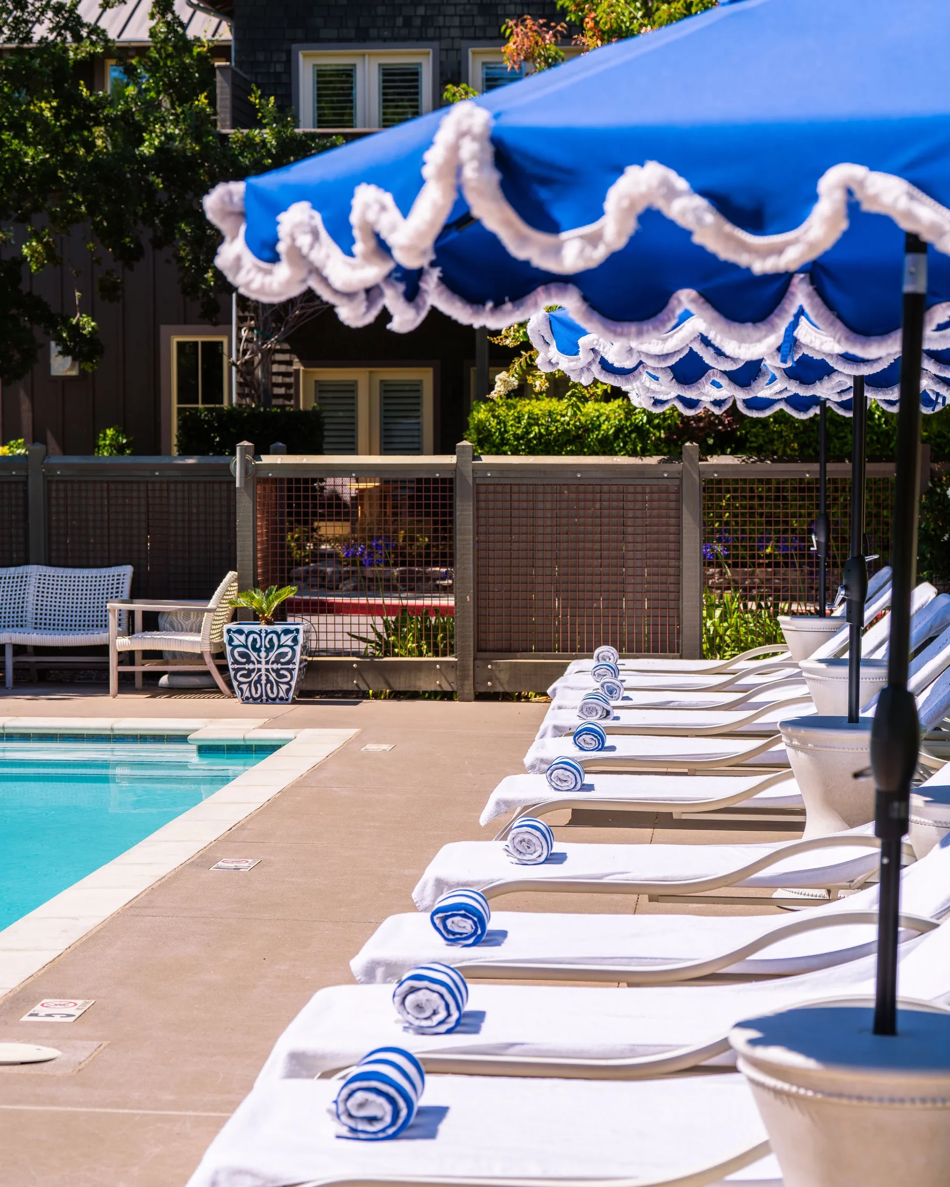 Poolside lounge chairs with rolled towels under a blue and white umbrella