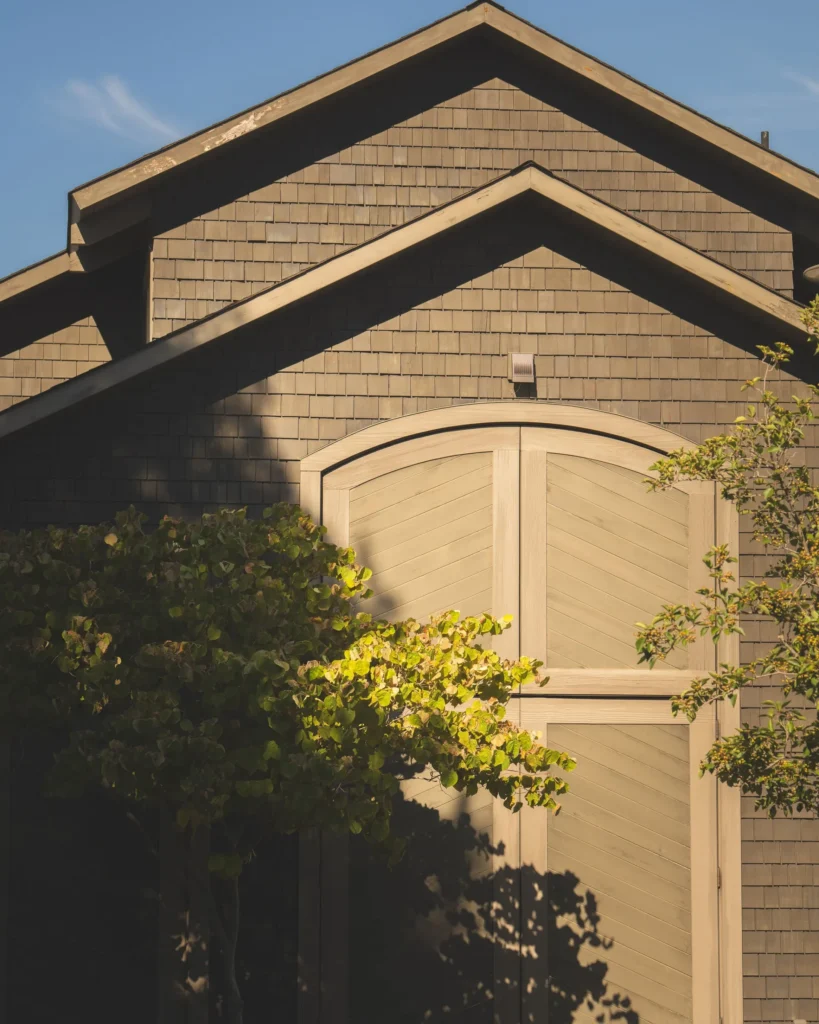 Shingled building facade with arched wooden doors and tree shadows