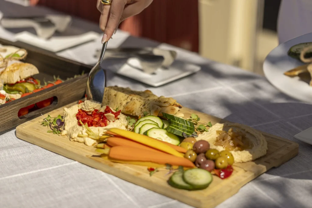 Hand serving hummus from a wooden appetizer platter with vegetables