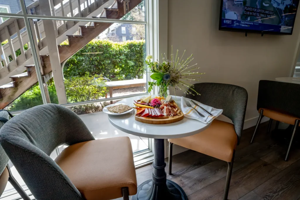 Charcuterie board on a table by a window with a view of stairs and greenery.