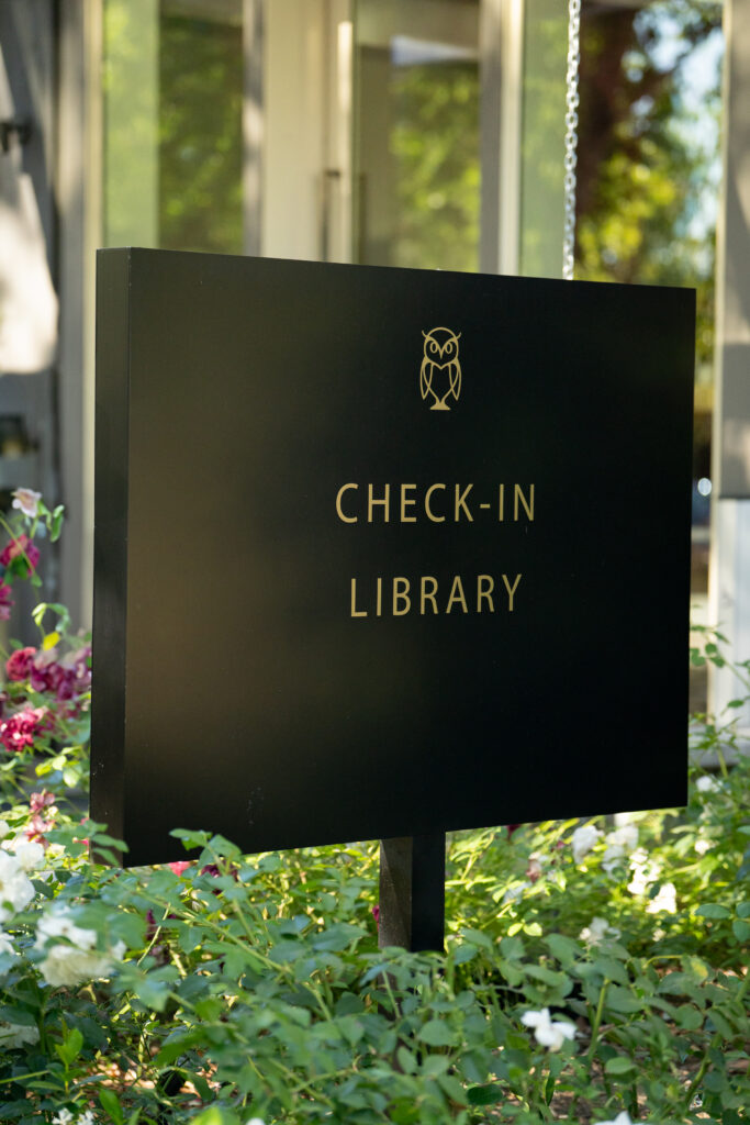 Black sign with gold owl logo reading Check-In Library