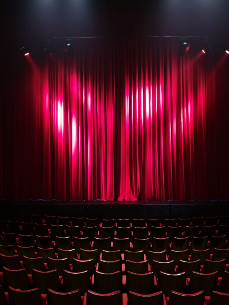 Interior of Uptown Theatre Napa featuring a stage with red velvet curtains, dramatic lighting, and auditorium seating before a live performance.